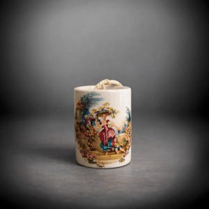 May include: A cream-coloured ceramic container with a cylindrical shape. It features a colourful pastoral scene with figures in period clothing. A twisted rope handle is attached to the top. The artwork includes pink, blue, and green hues.