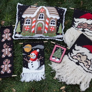 May include: A selection of handmade Christmas decorations, including a gingerbread house cushion, Santa Claus face hangings, a snowman banner, a gingerbread man banner, and a Christmas tree banner. The items are crocheted with various colours and textures.