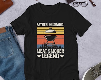 May include: Black t-shirt with a retro design featuring a grill and the text "Father. Husband. Meat Smoker Legend."