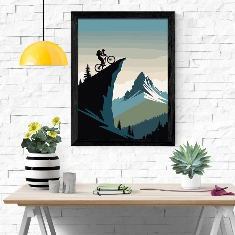 May include: A black framed poster featuring a mountain scene. A person is cycling on a cliff overlooking a mountain range. The sky is blue and the mountains are green and brown.