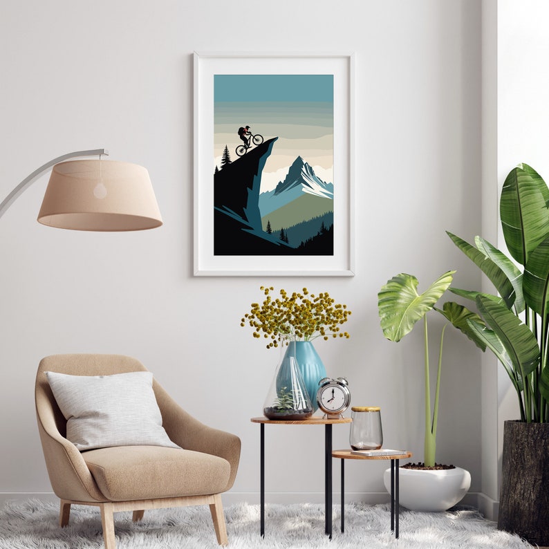 May include: A framed illustration of a mountain biker riding on a cliff overlooking a mountain range. The illustration is in a minimalist style with a blue, green, and brown colour palette.