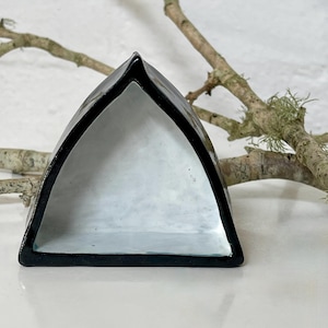 May include: A triangular ceramic dish with a black exterior and a white interior. The dish has a glossy finish and a minimalist design. A natural branch is in the background.