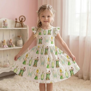 May include: A white dress with a whimsical fairy print. The dress features a pattern of fairies, bottles, and spools of thread in green, yellow, and white. The dress has short sleeves and a flared skirt, perfect for a young girl.