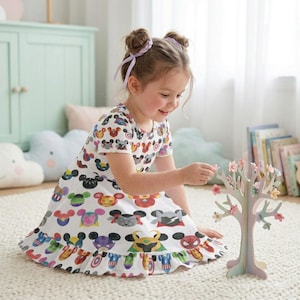 Könnte beinhalten: Ein weißes Kleid mit einem bunten Muster aus Mickey Mouse- und Marvel-Charaktergesichtern. Das Kleid hat kurze Ärmel und einen Rüschensaum. Ein junges Mädchen spielt mit einem dekorativen Baum mit rosa Blüten.