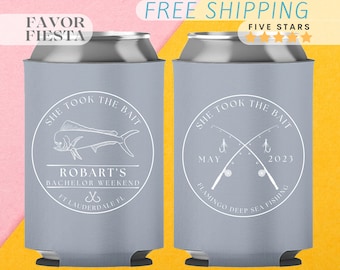 Op de afbeelding: Twee grijze koelers voor blikjes met witte tekst en afbeeldingen. De eerste koeler zegt "She took the bait" met een dolfijn afbeelding en "Robart's Bachelor Weekend Ft. Lauderdale FL". De tweede koeler zegt "She took the bait" met een afbeelding van gekruiste hengels en "May 2023 Flamingo Deep Sea Fishing".