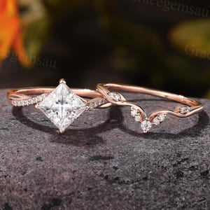 May include: A rose gold engagement ring set. The engagement ring features a princess-cut diamond and a twisted band with small accent stones. The wedding band has a curved design with small accent stones. The rings are displayed on a dark gray surface.