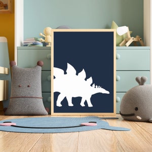 May include: A framed print with a white silhouette of a stegosaurus dinosaur on a dark blue background. The print is hanging on a wall in a child's room.