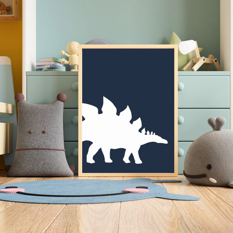 May include: A framed print with a white silhouette of a stegosaurus dinosaur on a dark blue background. The print is hanging on a wall in a child's room.