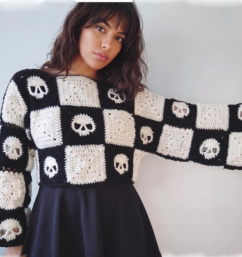 May include: A long-sleeved crochet sweater featuring a checkerboard pattern of alternating black and white squares. The white squares are decorated with a detailed skull motif, while the black squares are solid. The sweater has a crew neckline.