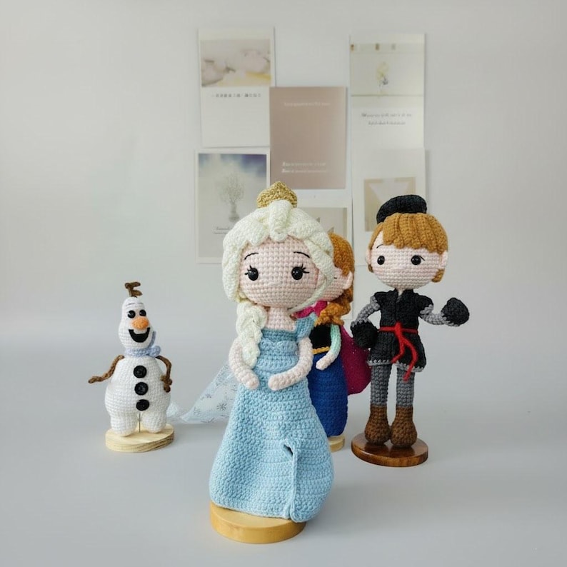 K&ouml;nnte beinhalten: Geh&auml;kelte Puppen von Figuren aus dem Film Frozen, darunter Elsa in einem blauen Kleid, Anna in einem blauen Kleid, Kristoff in einem schwarzen Outfit und Olaf, der Schneemann. Die Puppen sind handgefertigt.
