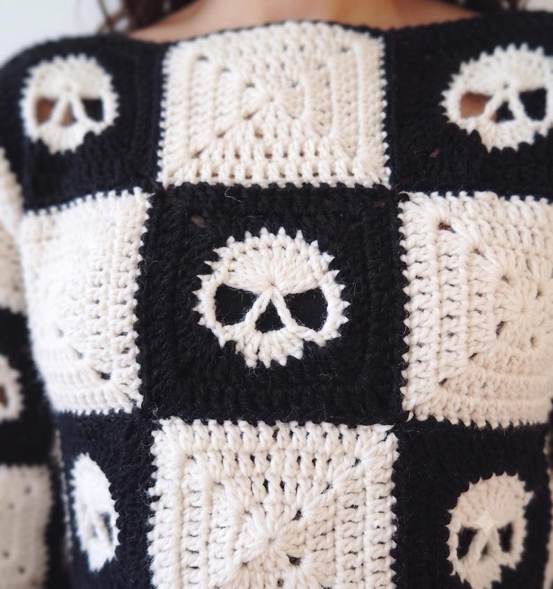 May include: A long-sleeve sweater constructed from alternating black and off-white crocheted granny squares. The design features a repeating pattern of skull motifs integrated into the squares, creating a checkerboard effect across the garment.