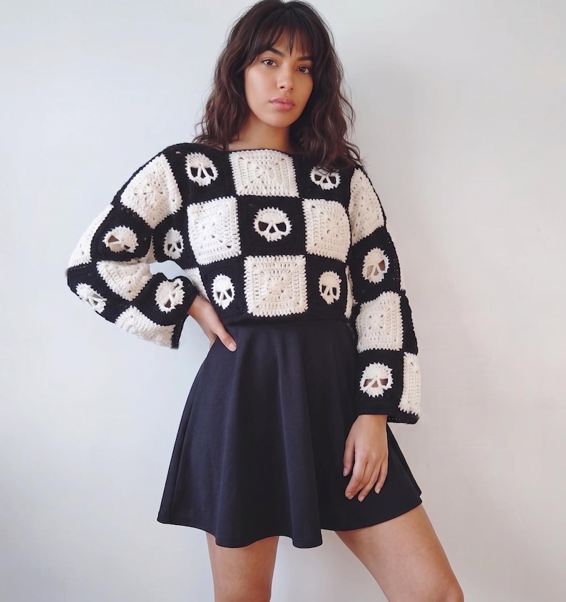 May include: A long-sleeved crochet sweater featuring a black and white checkerboard pattern with skull motifs integrated into the squares, paired with a solid black skater skirt. The sweater has a boxy fit and wide sleeves.