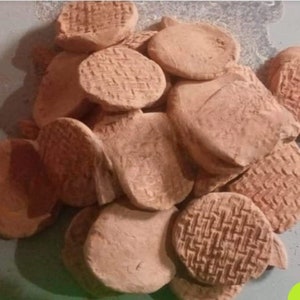 May include: A pile of terracotta clay discs, some with a woven pattern, others smooth. The discs are various sizes and shapes, with a light brown colour.