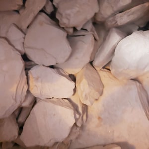 May include: A close-up of a pile of white, irregularly shaped slate rock pieces. The rock has a rough, textured surface.