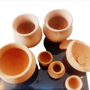 May include: A set of six terracotta clay pots of varying sizes. The pots are all a reddish-brown colour and have a smooth, slightly textured surface. Some of the pots are cracked or chipped.
