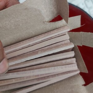 May include: A cardboard box containing a stack of light pink rectangular slate pencils. The pencils are arranged in a fan shape.