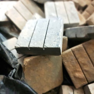 May include: A pile of small, rectangular tiles in various shades of brown and grey. Some tiles have a grooved texture.