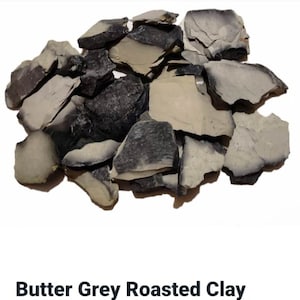 May include: A pile of butter grey roasted clay, broken into irregular pieces. The clay is a light grey colour with darker grey streaks.