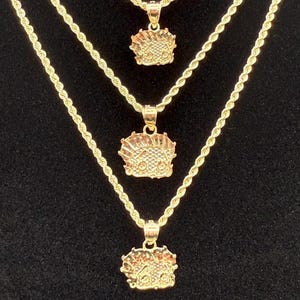 May include: Three gold rope chains with matching pendants. The pendants are all the same design, featuring a detailed face with a crown. The chains are layered on top of each other, with the shortest chain at the top and the longest chain at the bottom.