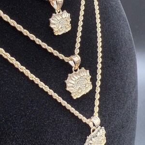 May include: Three gold rope chains with matching pendants. Each pendant features a detailed design of a stylized face.