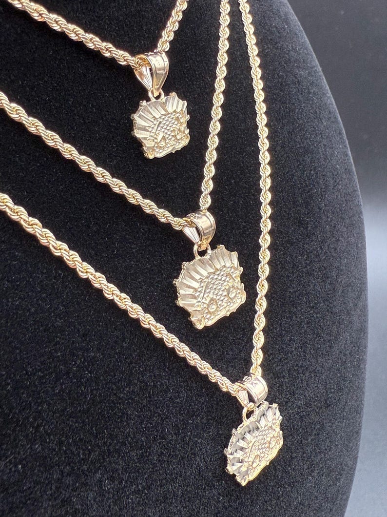May include: Three gold rope chains with matching pendants. Each pendant features a detailed design of a stylized face.