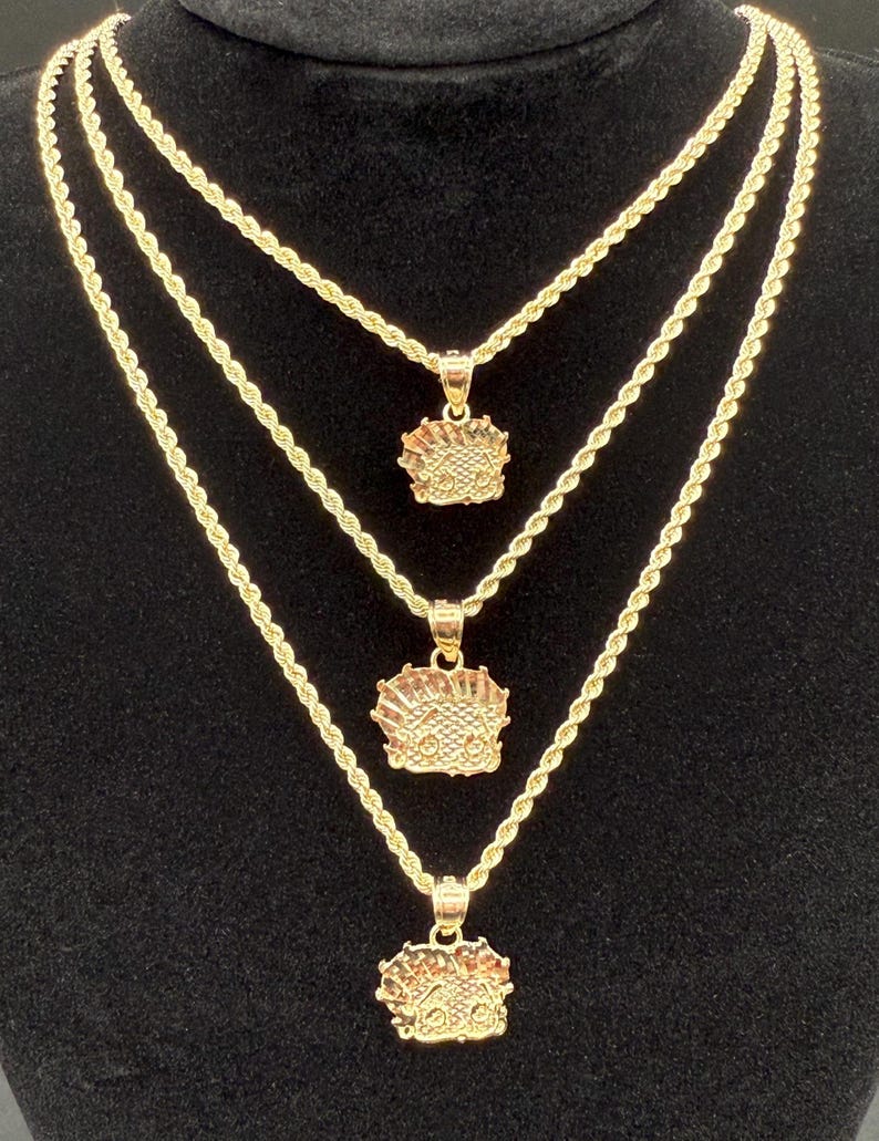 May include: Three gold rope chains with matching pendants. The pendants are all the same design, featuring a detailed face with a crown. The chains are layered on top of each other, with the shortest chain at the top and the longest chain at the bottom.