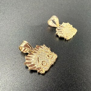 May include: Two gold-colored pendants in the shape of a lion's head. The pendants are detailed with a textured surface and have a loop at the top for attaching to a chain.
