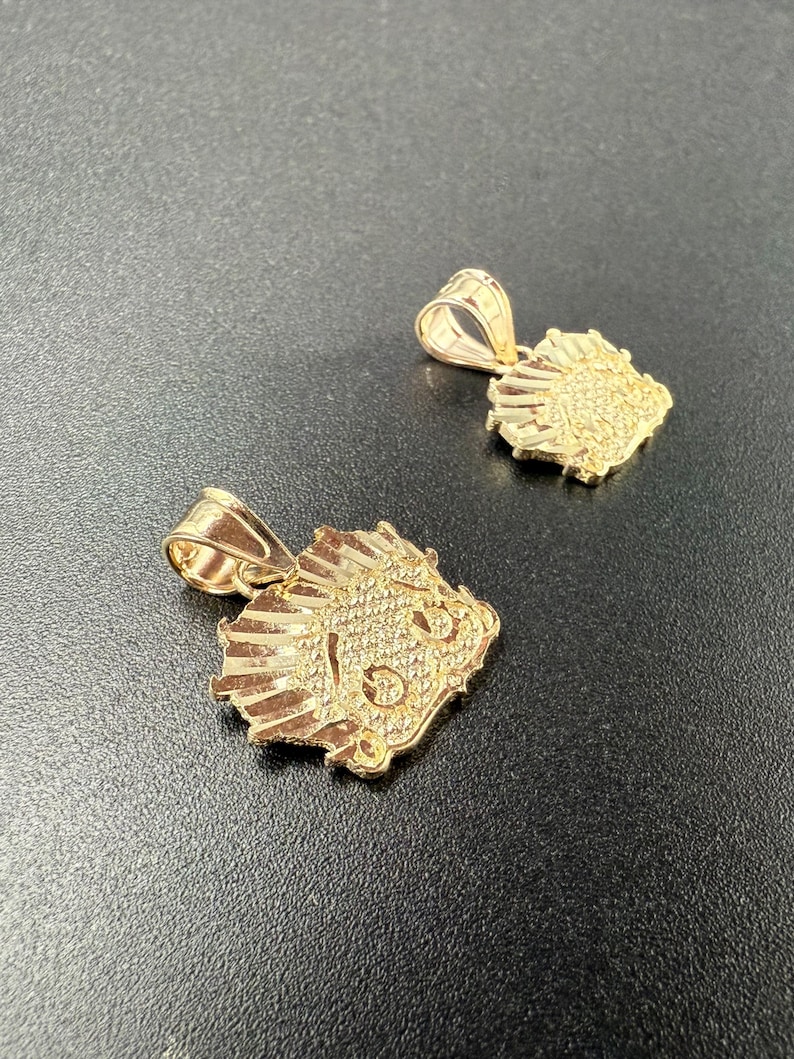 May include: Two gold-colored pendants in the shape of a lion's head. The pendants are detailed with a textured surface and have a loop at the top for attaching to a chain.