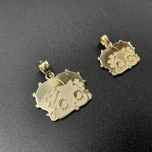 Pu&ograve; includere: Due ciondoli color oro con un design a personaggio dei cartoni animati. I ciondoli hanno un anello nella parte superiore per una catena. Il personaggio ha un viso e dei capelli dettagliati. I ciondoli sono su uno sfondo scuro.