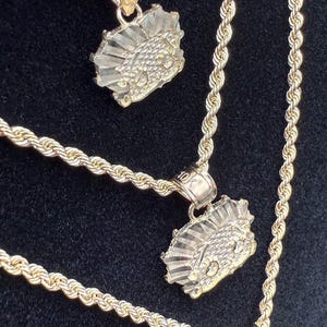 May include: Three gold rope chains with matching pendants. The pendants are a stylized design of a face with a crown.
