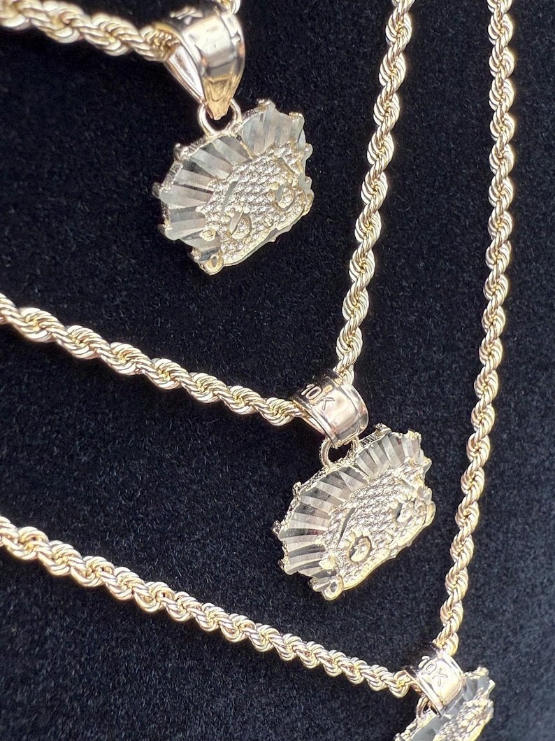 May include: Three gold rope chains with matching pendants. The pendants are a stylized design of a face with a crown.