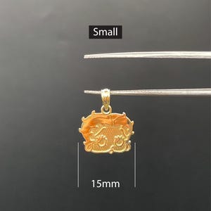 Pu&ograve; includere: Un piccolo ciondolo dorato, di circa 1,5 cm, con un design dettagliato. Il ciondolo &egrave; tenuto da una pinzetta su uno sfondo scuro. La parola "Small" &egrave; visualizzata sopra il ciondolo.