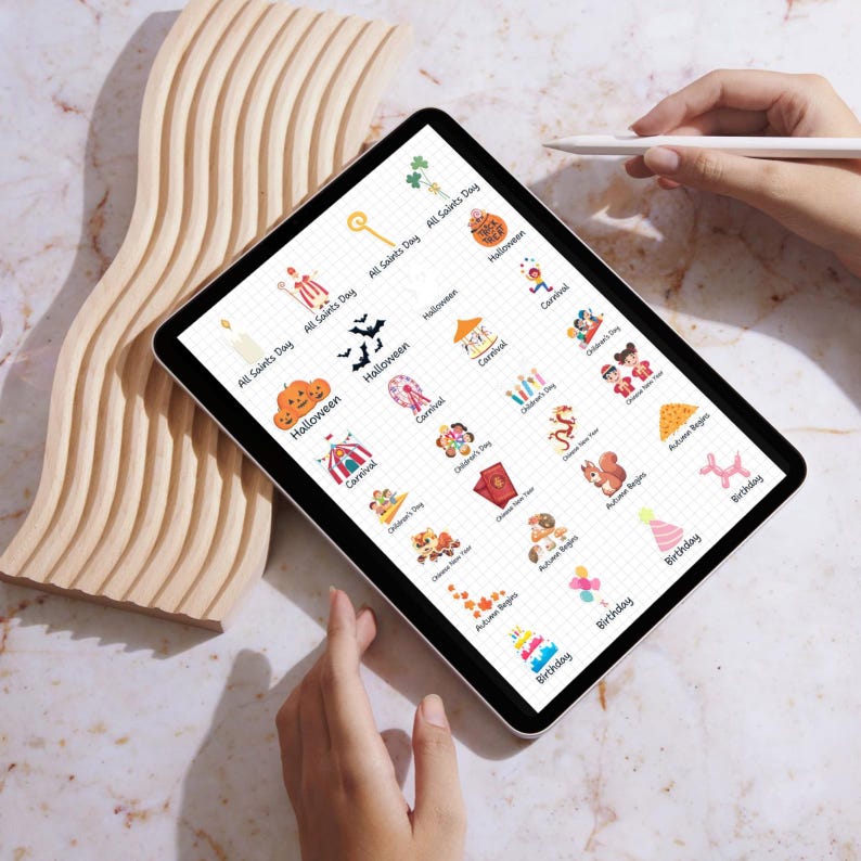 May include: A digital tablet screen displaying a grid of colorful icons representing different holidays and events, including Halloween, Carnival, Children's Day, Autumn Begins, and Birthday. Each icon is accompanied by the corresponding holiday or event name.
