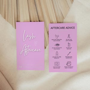 Peut inclure: Deux cartes rectangulaires roses présentant des instructions de soin pour les cils. La carte de gauche affiche le texte Lash Aftercare et un cœur. La carte de droite liste des conseils avec des icônes pour garder les cils au sec et éviter le mascara.