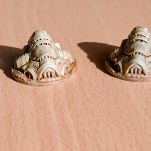 Könnte beinhalten: Vier kleine, cremefarbene, architektonische Skulpturen sind auf einer hellbraunen Oberfläche angeordnet. Jede Skulptur hat ein detailliertes, geschichtetes Design mit einem abgerundeten Sockel und einer Reihe von gestapelten, geometrischen Formen. Die Skulpturen werfen Schatten.