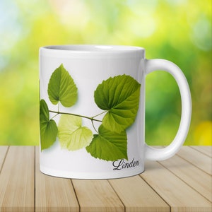 May include: White ceramic mug with a green leaf design and the word "Linden" printed on the bottom.