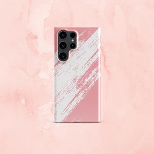 Puede incluir: Una funda de teléfono rosa con un diseño de pinceladas blancas. La funda tiene un recorte para la cámara con cuatro lentes.