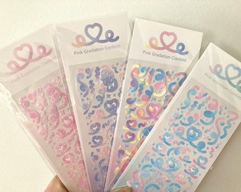 Peut inclure: Quatre feuilles de confettis adhésifs à dégradé rose avec un motif en forme de cœur et le texte "Pink Gradation Confetti". Les confettis sont de formes et de tailles variées, notamment des cœurs, des étoiles et des volutes. Les confettis sont irisés et ont une finition holographique.