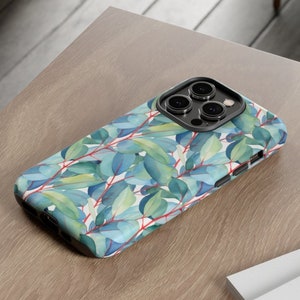 May include: A phone case with a watercolor design of green leaves on a white background. The case has a black camera bump with three lenses.