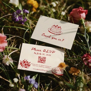May include: Two cream wedding invitation cards with red text and illustrations, including a cake and flowers, are set in grass with flowers. One card reads "Count you in?" and the other says "Please RSVP by July 30, 2025."