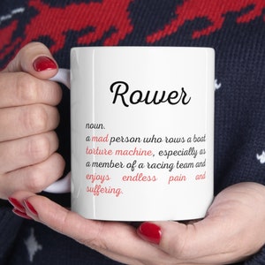 Puede incluir: Taza de cerámica blanca con un diseño en negro y rojo. La taza presenta la palabra "Rower" en texto negro y una definición de la palabra en texto rojo. La definición dice: "nombre. una persona loca que rema un bote máquina de tortura, especialmente como miembro de un equipo de carreras y disfruta del dolor sin fin y el sufrimiento."
