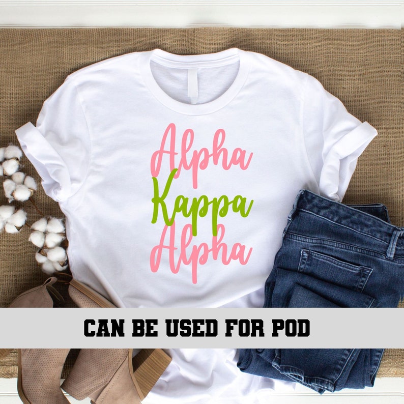 May include: White t-shirt with the text "Alpha Kappa Alpha" in pink and green lettering.
