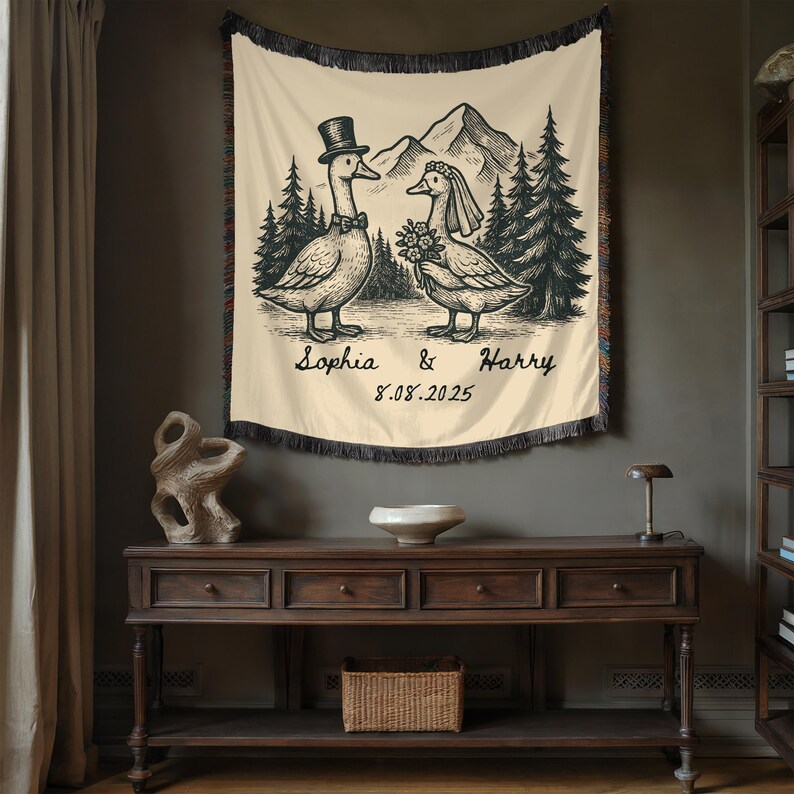 May include: Cream-colored tapestry with a black and white illustration of two geese dressed for a wedding, with a mountain and forest backdrop. The names "Sophia & Harry" and the date "8.08.2025" are written below the geese.