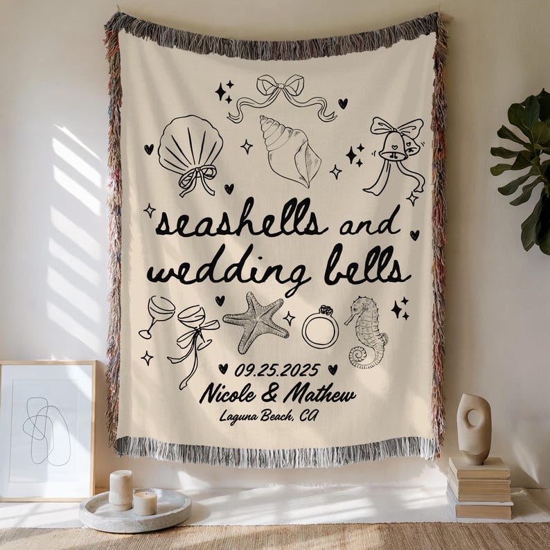 May include: Cream-colored woven throw blanket with black line art of seashells, wedding bells, and other wedding-themed illustrations. The text "seashells and wedding bells" is displayed, along with a wedding date and names.