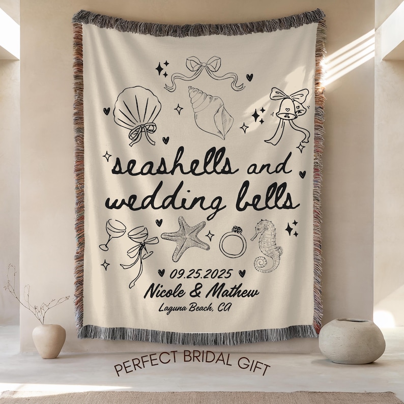 May include: Cream-colored woven throw blanket with black line art of seashells, wedding bells, and other wedding-themed illustrations. The text reads "seashells and wedding bells" with a date and names. The bottom text says "PERFECT BRIDAL GIFT".