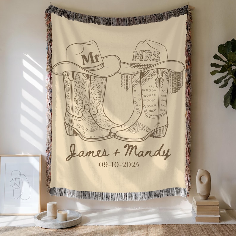 Pu&ograve; includere: Coperta color crema con un disegno a tratto di stivali e cappelli da cowboy. I cappelli recitano "Mr" e "Mrs". La coperta &egrave; personalizzata con i nomi "James + Mandy" e la data "09-10-2025". La coperta ha un bordo sfrangiato.