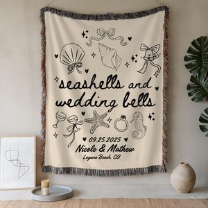 May include: Cream-colored woven throw blanket with black line art of seashells, wedding bells, and other wedding-themed illustrations. The text "seashells and wedding bells" is displayed, along with a date and names.