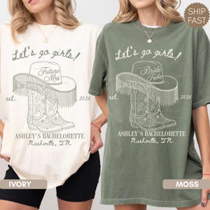 Op de afbeelding: Ivoor en mosgroene t-shirts met een ontwerp voor een vrijgezellenfeest. Het ontwerp bevat een cowboyhoed, laarzen en de tekst "Let's go girls!" en "Ashley's Bachelorette Nashville, TN."