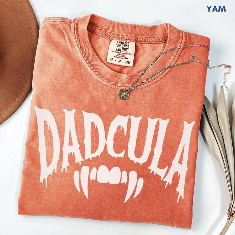 YAM Comfort Colors Dadcula shirt featuring a white vampire-inspired graphic with fangs, funny Halloween dad tee for spooky season, Halloween parties, family outfits, and gifts for dad.