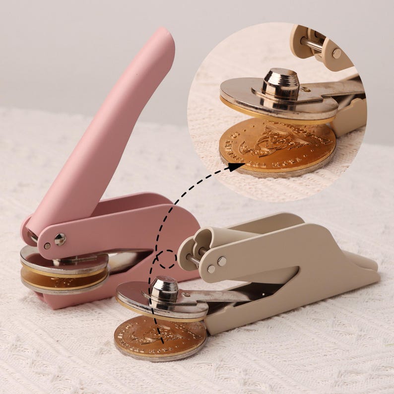 May include: Two handheld wax seal stampers, one pink and one beige, with gold-toned metal seals. The seals have a decorative design.